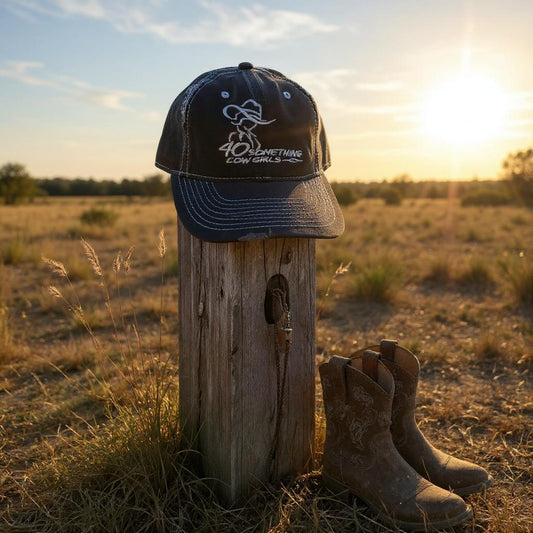 Navy cap with logo and text on a wooden post in a field with boots at sunset